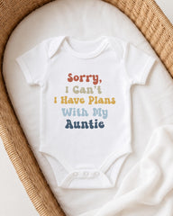 A white baby onesie with text printed on it, placed in a woven basket.