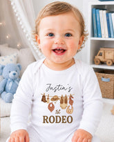 A smiling baby boy wearing a white onesie with a personalized text and graphic design.