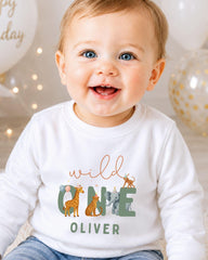 A smiling baby boy wearing a white shirt with a graphic of wild animals and the name "Olivier" printed on it.