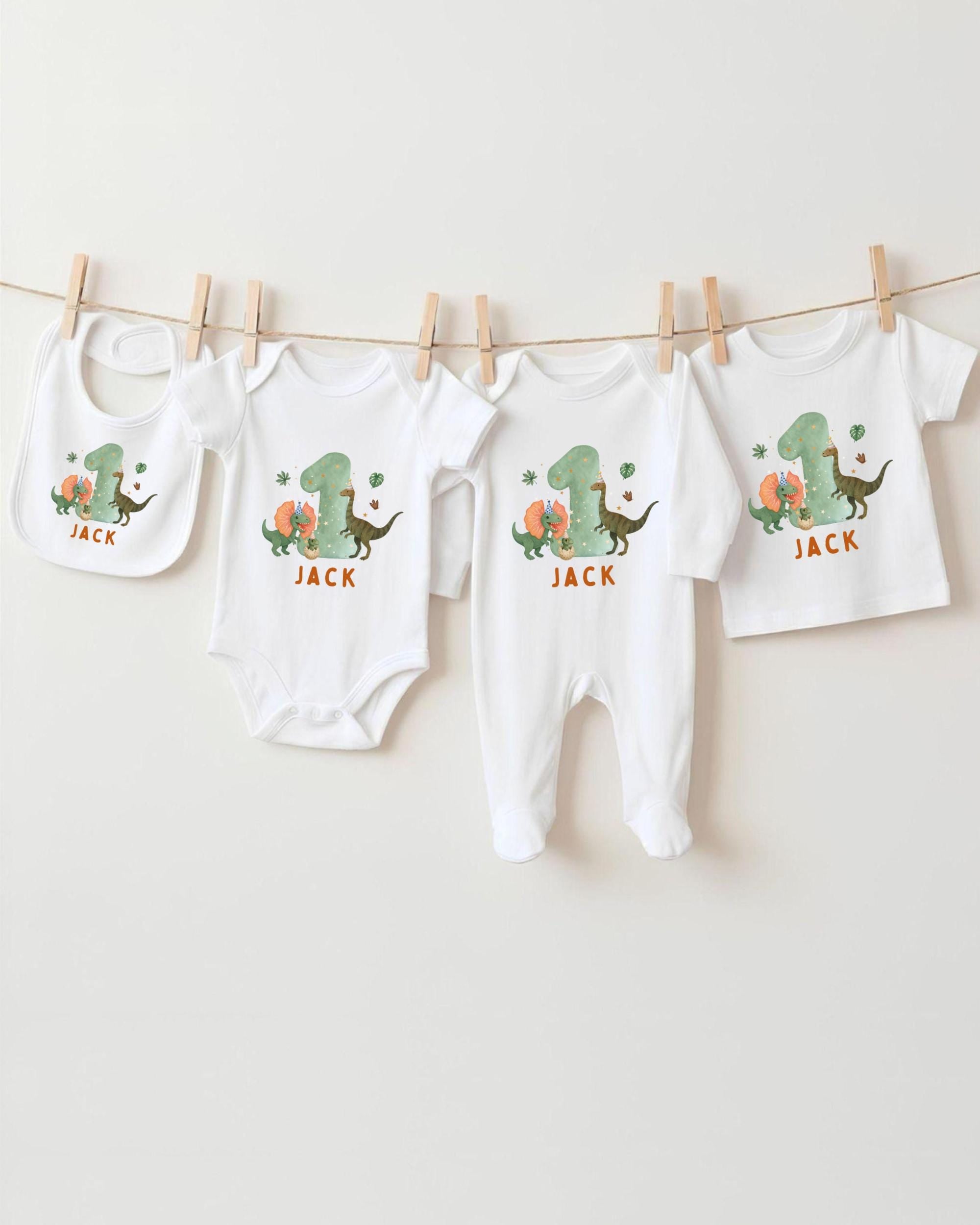 A collection of white baby clothes, including onesies and pajamas, with dinosaur designs and the name "Jack" printed on them.
