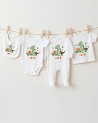 A collection of white baby clothes, including onesies and pajamas, with dinosaur designs and the name "Jack" printed on them.