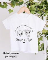 A white t-shirt with a graphic design featuring two dog heads and the text "Loved & Protected by Bruno & Hugo" printed on it.