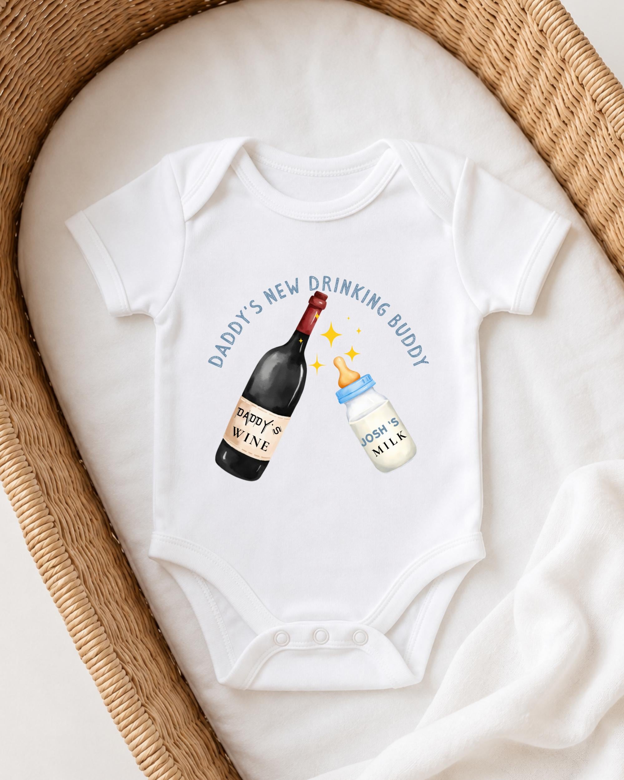 A white onesie with a graphic design depicting a bottle of wine and a bottle of milk, accompanied by the text "DADDY'S NEW DRINKING BUDDY".