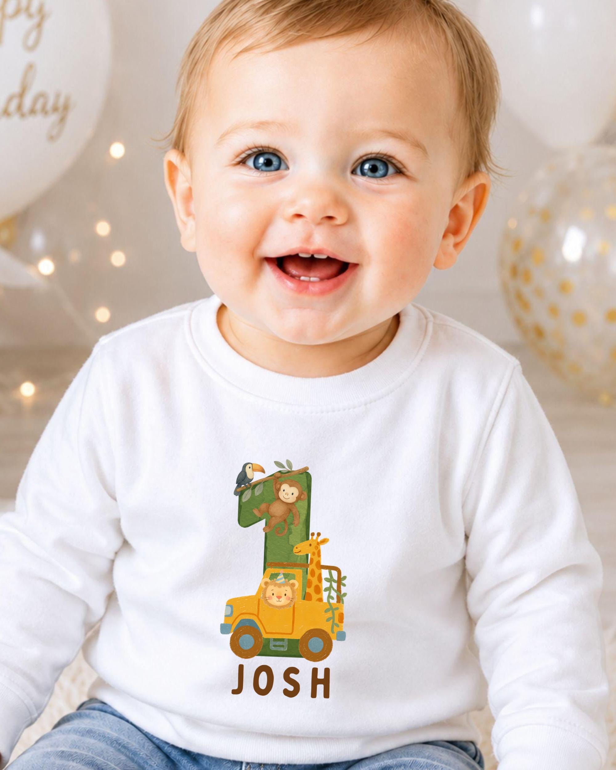 A smiling baby boy wearing a white shirt with a cartoon image of a car and the name " Josh" printed on it.