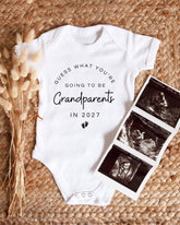A white baby onesie with text that says "Guess what, you're going to be grandparents in 2027" is displayed alongside three black and white images of an Ultrasound scan of a baby's head.