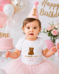 A young girl wearing a birthday hat and a white t-shirt with a teddy bear design is posing for a birthday photo.