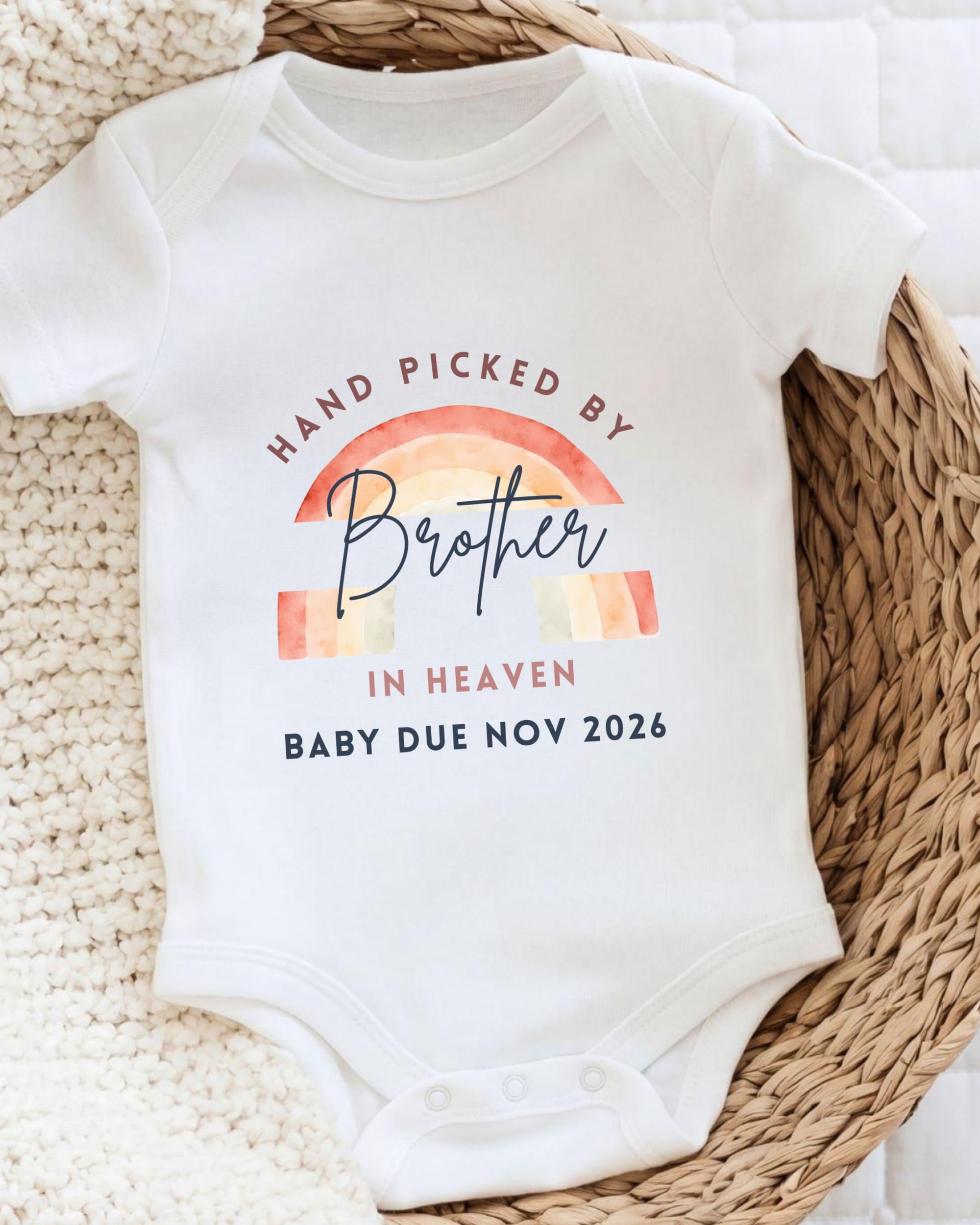 A white baby onesie with a graphic design and text that reads "Hand picked by Brother in Heaven Baby due Nov 2026".