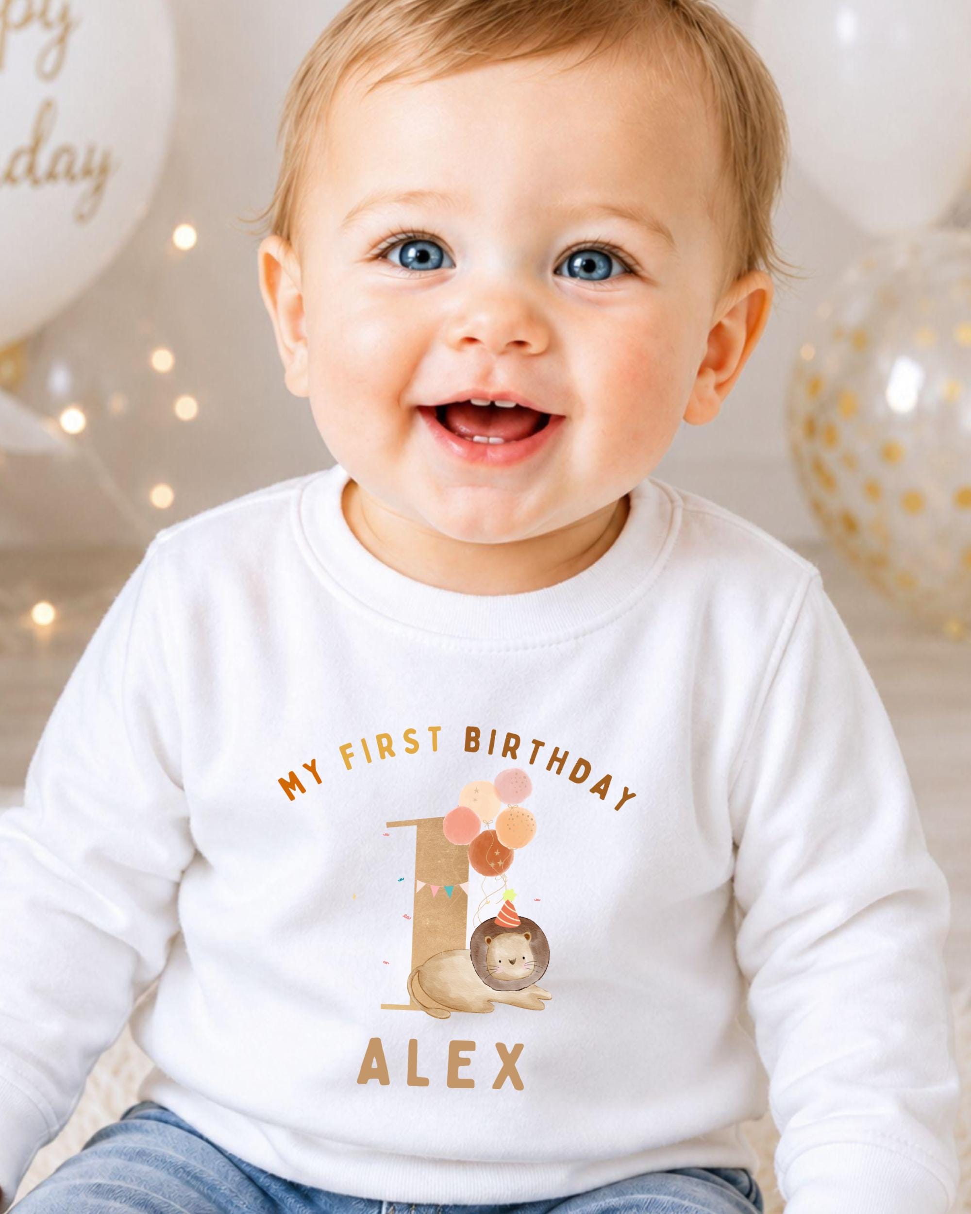 A smiling baby boy wearing a white shirt with a birthday message and a cartoon character.