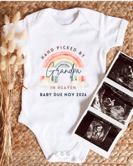A white baby onesie with a rainbow graphic and text that says "Hand picked by Grandpa in Heaven" and "Baby due Nov 2026". Next to the onesie is a set of three black and white baby ultrasound images.