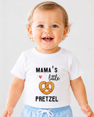 A smiling baby wearing a white t-shirt with a graphic of a pretzel and the text "MAMA'S little PRETZEL" printed on it.