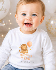 A smiling baby wearing a white shirt with a cartoon lion and the text "Half Way to One" and "SIMBA" printed on it.