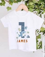 A white t-shirt with a graphic design featuring a shark and bubbles, along with the name "James" printed on it.