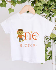 A white t-shirt with a cartoon character and the text "HUXTON" printed on it, hanging on a wooden hanger.