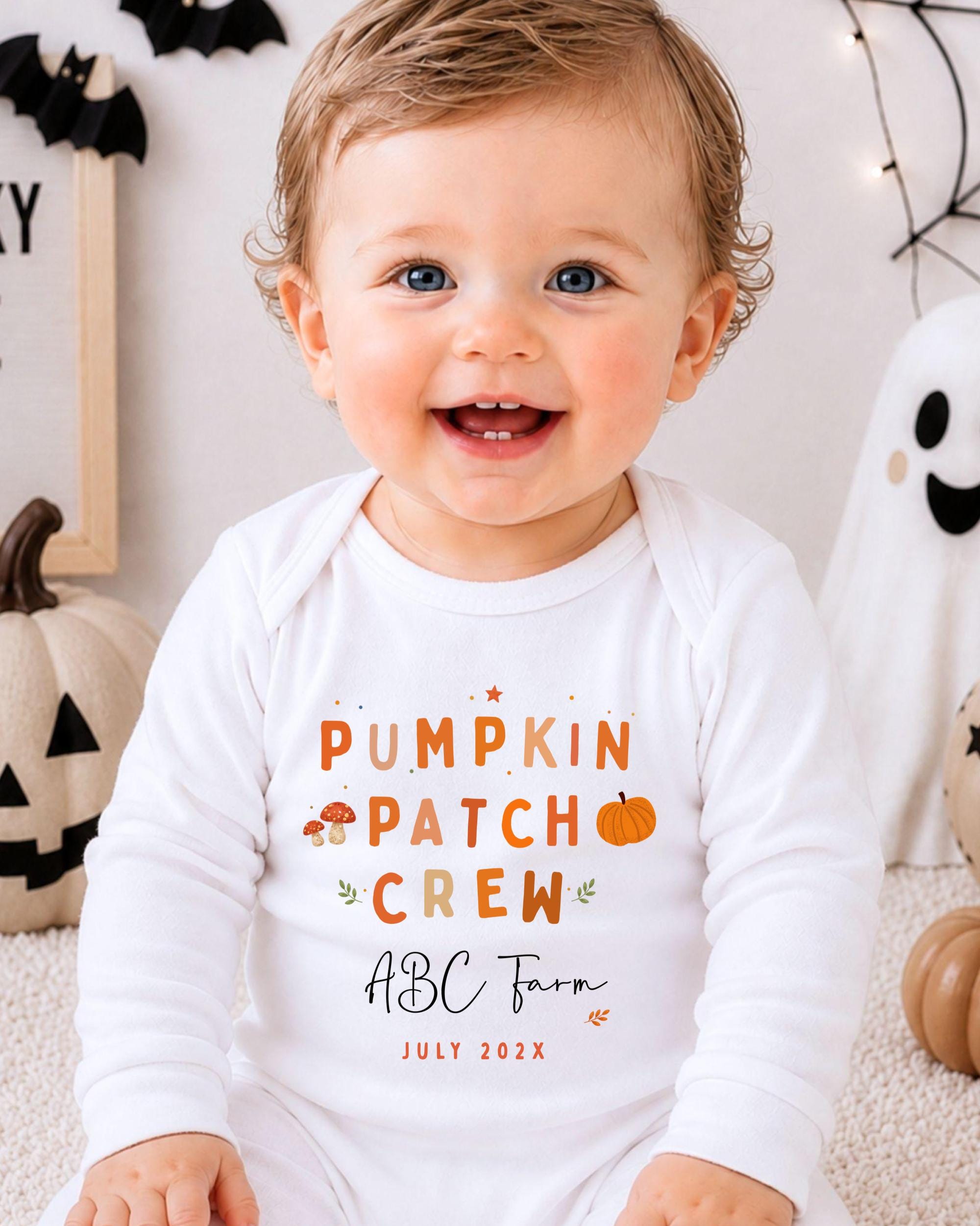 A smiling baby wearing a white onesie with text and graphics related to the ABC Farm pumpkin patch crew.