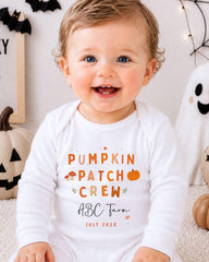 A smiling baby wearing a white onesie with text and graphics related to the ABC Farm pumpkin patch crew.