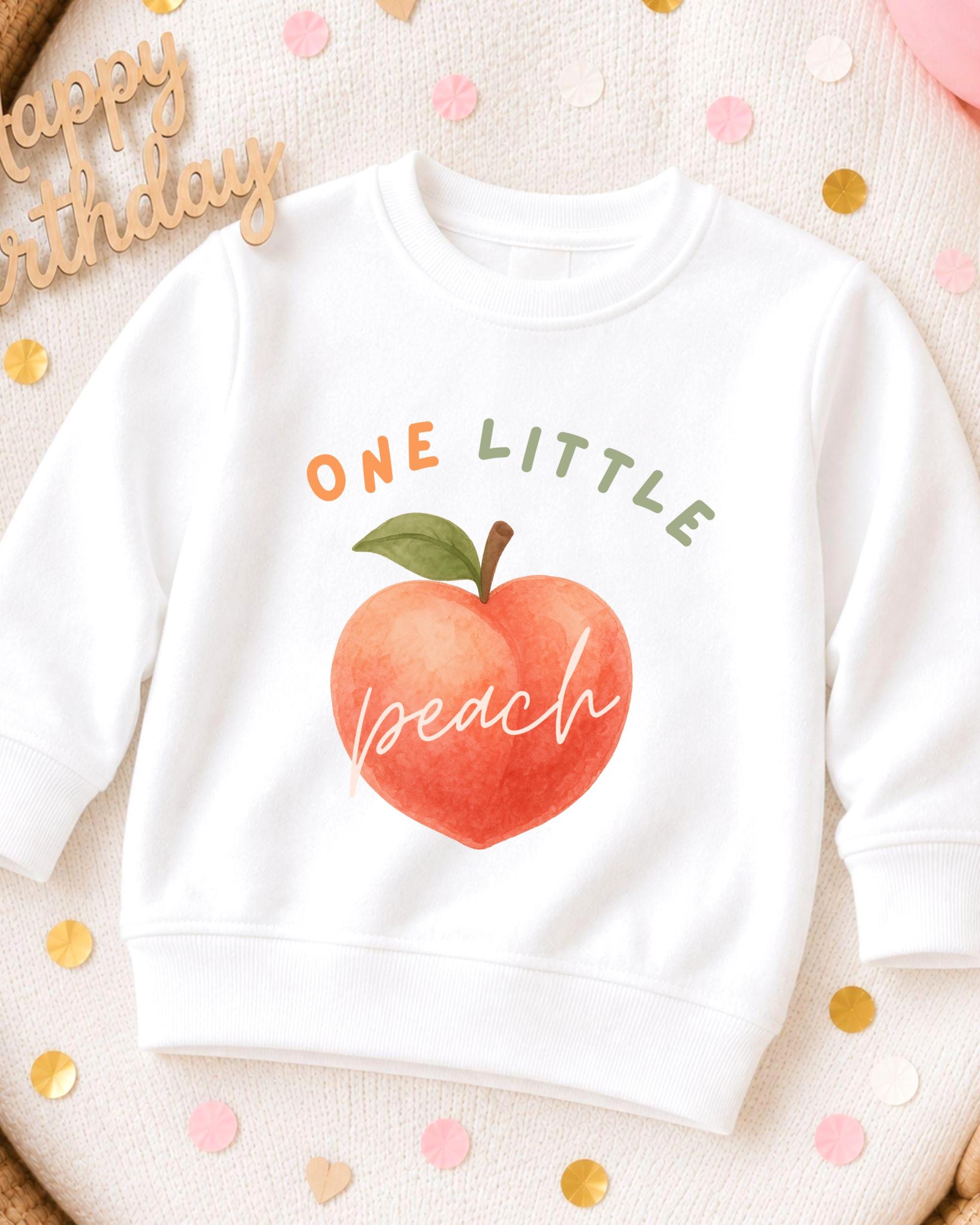 A white sweatshirt with a peach graphic and the text "ONE LITTLE peach" printed on it, surrounded by confetti.