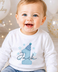 A smiling baby boy wearing a white shirt with a blue hat and stars, with the name "Jack" written on it.