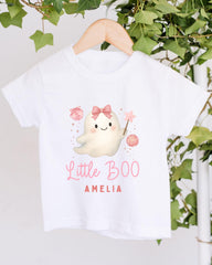 A white t-shirt with a cartoon ghost character and text printed on it, hanging on a wooden hanger.
