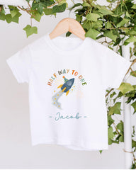 A white t-shirt with a colorful graphic design and text, hanging on a wooden hanger.