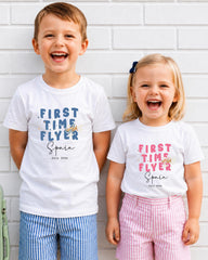 Two children, a boy and a girl, are standing next to each other and smiling, wearing matching white t-shirts with text and graphics.
