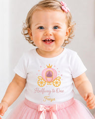 A smiling baby girl wearing a white t-shirt with a princess-themed design and a pink tutu skirt.