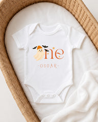 A white onesie with a ghost and the text "One Oscar" printed on it, placed in a wicker basket.