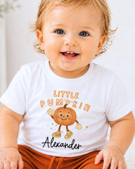 A smiling baby wearing a white t-shirt with a pumpkin character and the text "Little Pumpkin Alexander" printed on it.