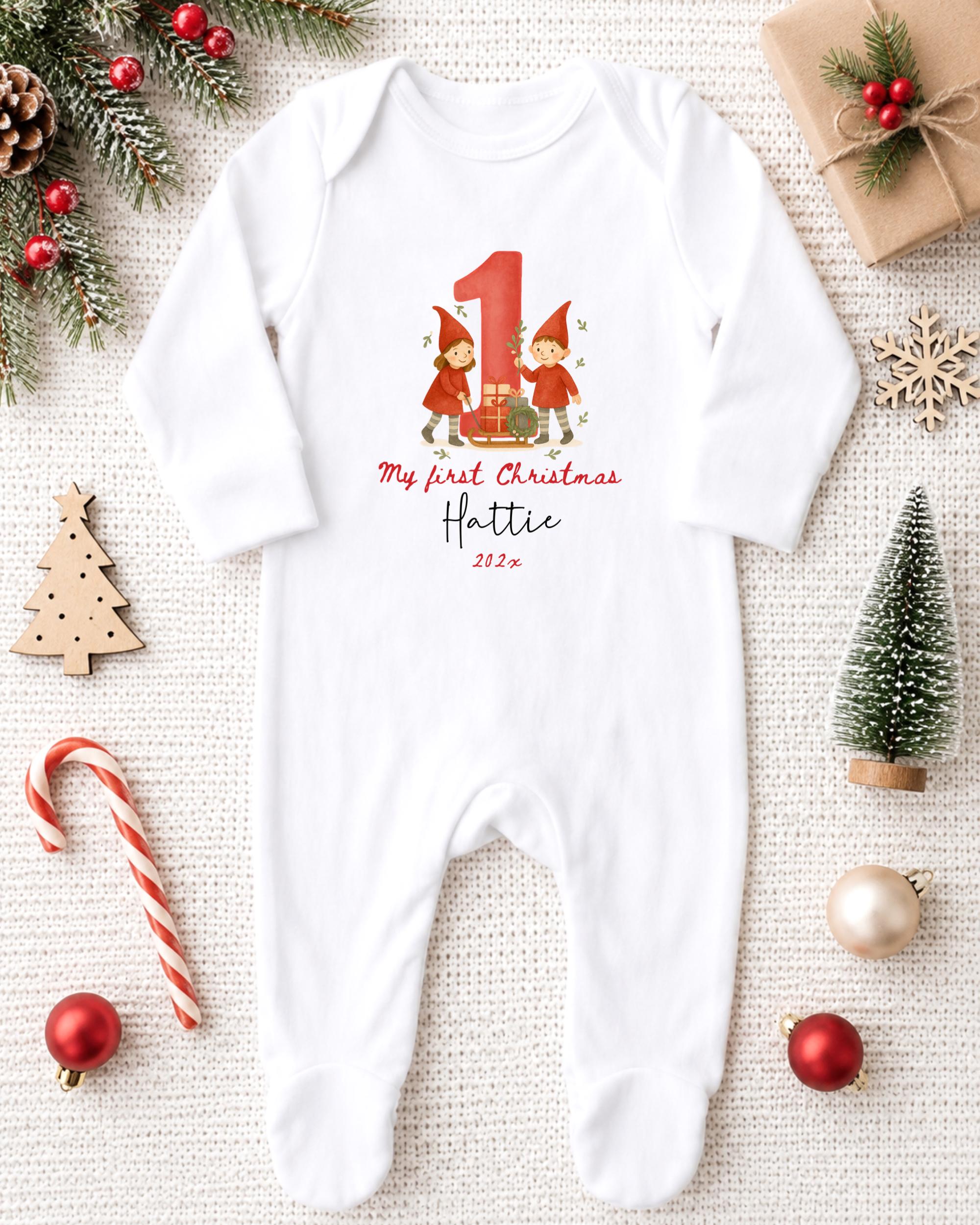 A white onesie with a red number 1 and a small illustration of two gnomes is displayed on a white background, surrounded by Christmas decorations and gifts.
