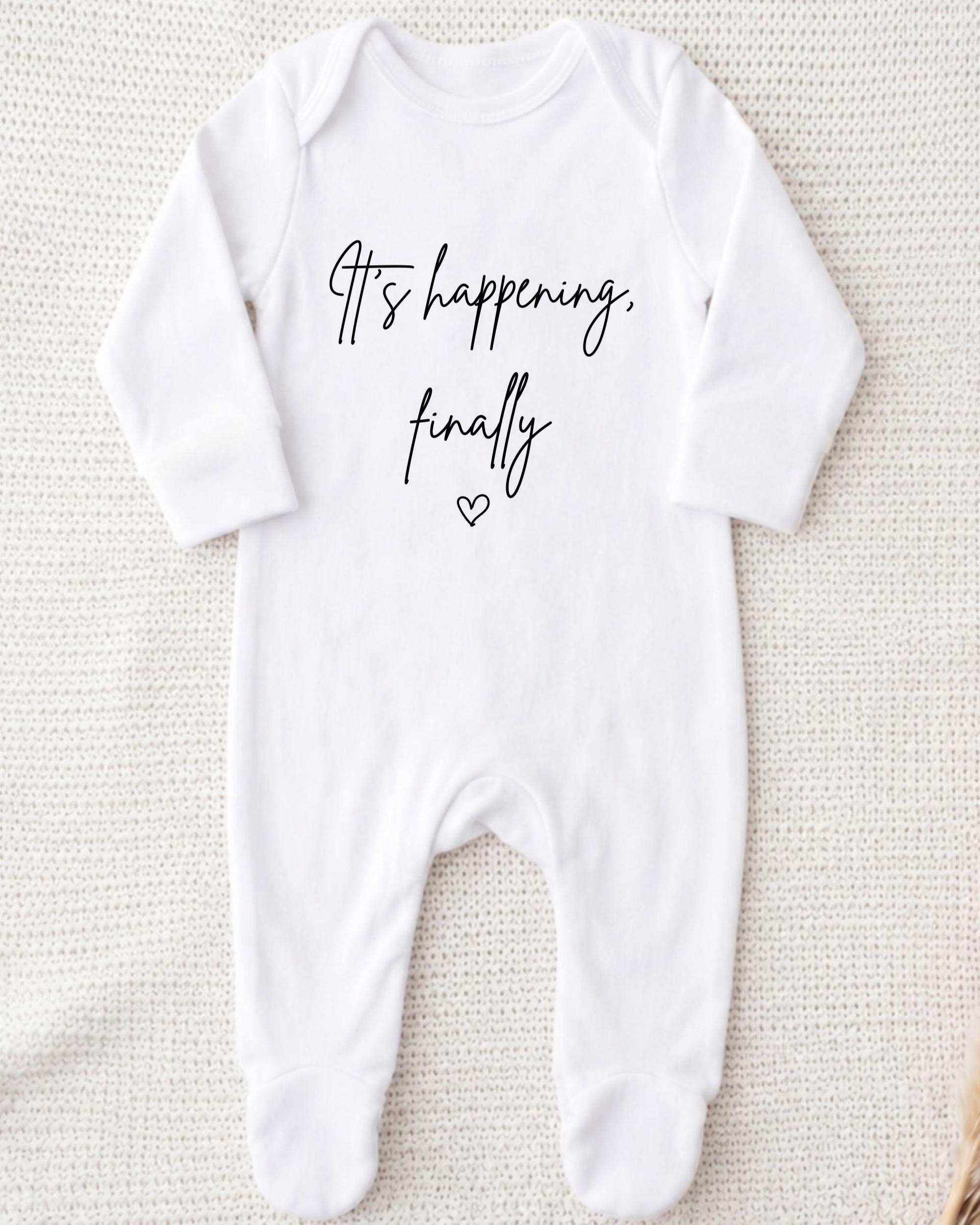 A white onesie with the text "It's happening, finally" printed on it.