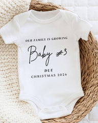 A white baby onesie with text printed on it, placed on a woven basket.