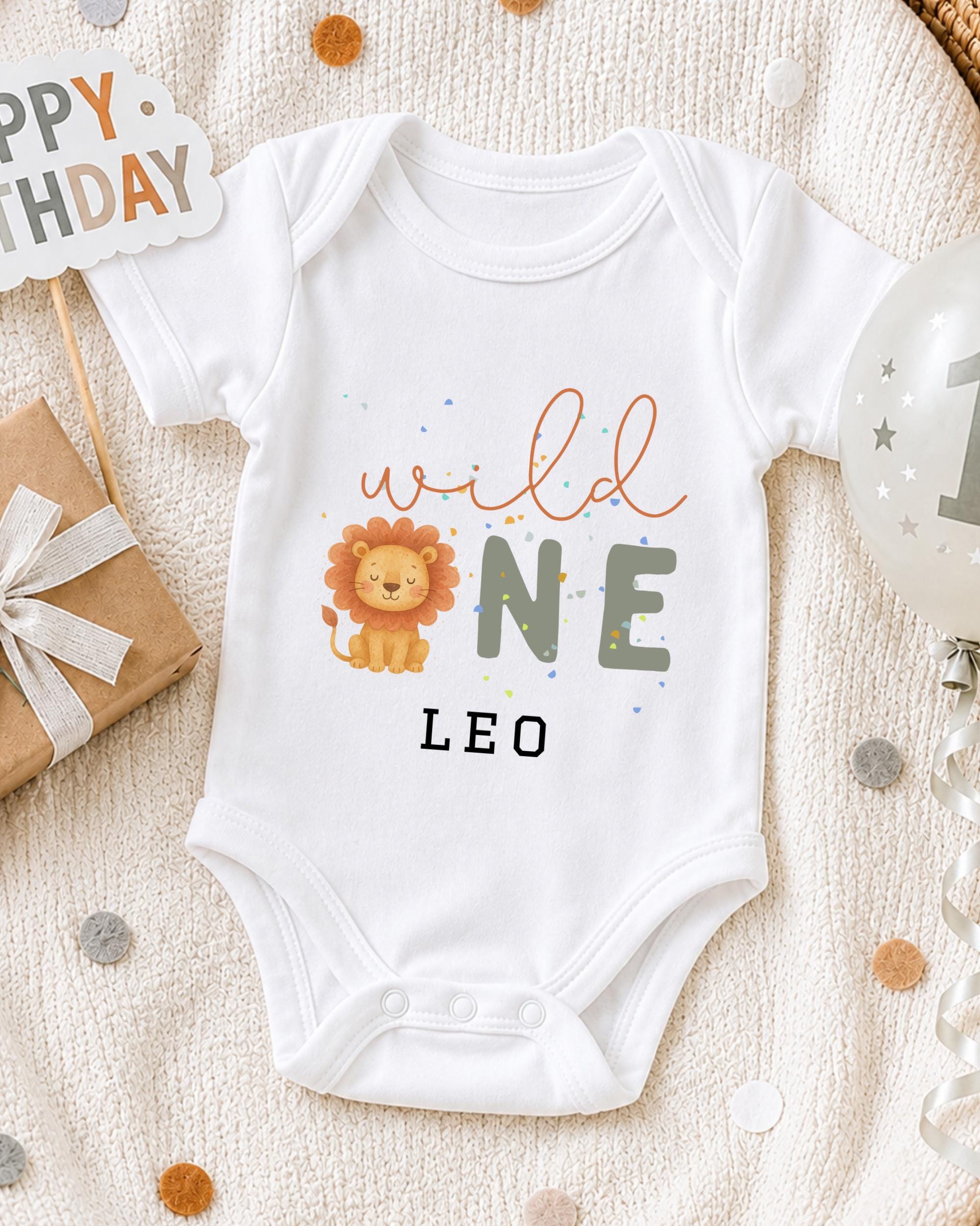 A white onesie with a lion design and the text "wild one leo" printed on it, along with a "Happy Birthday Leo" sign and a birthday balloon.