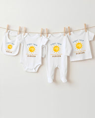 A collection of baby clothes, including onesies and bibs, hanging on a clothesline.