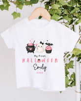 A white t-shirt with a Halloween-themed graphic design hanging on a wooden hanger.