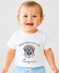 A smiling baby wearing a white t-shirt with a graphic of a dog and the text "PROTECTED BY Cooper" printed on it.