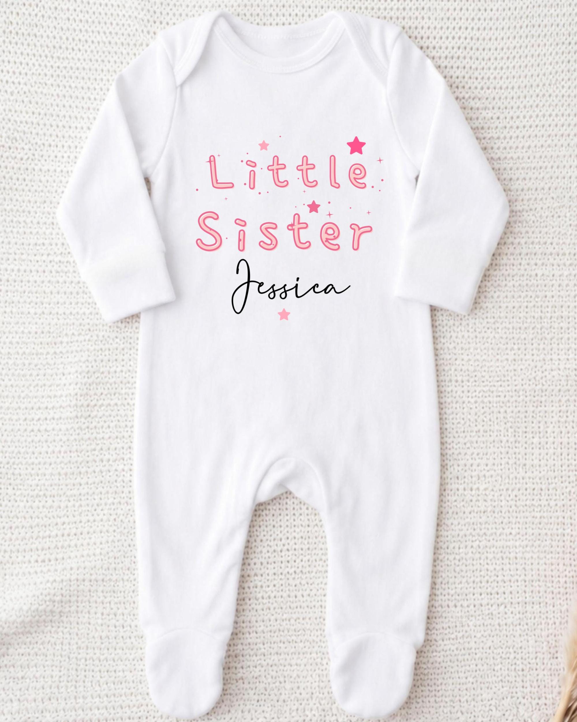 A white onesie with the text "Little Sister Jessica" printed on it.