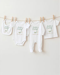 A row of white baby clothes with the name "Little Caddy" printed on them, along with a golf club and the name "Patricks" printed below.