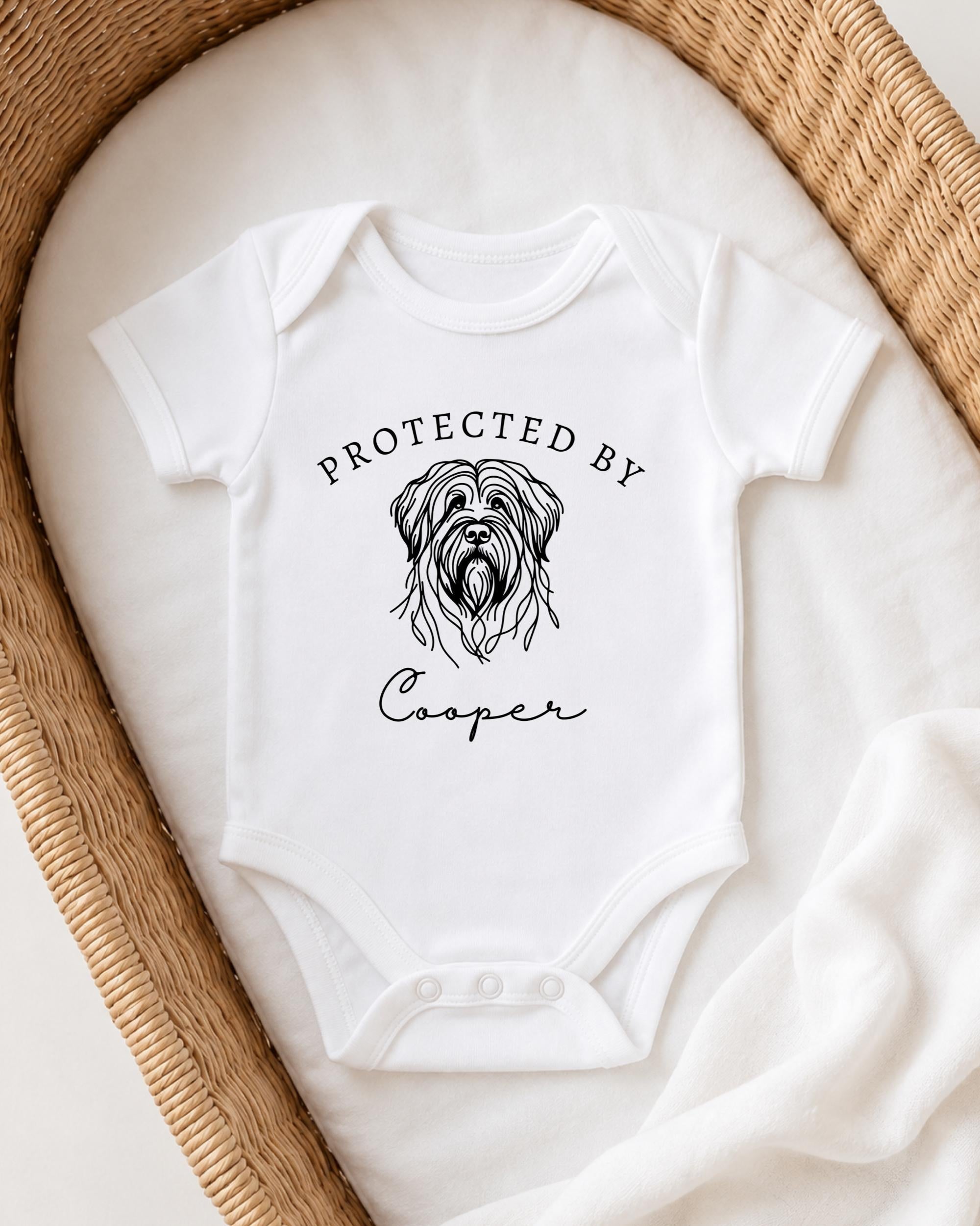 A white baby onesie with a graphic of a dog's head and the text "Protected by Cooper" printed on it.