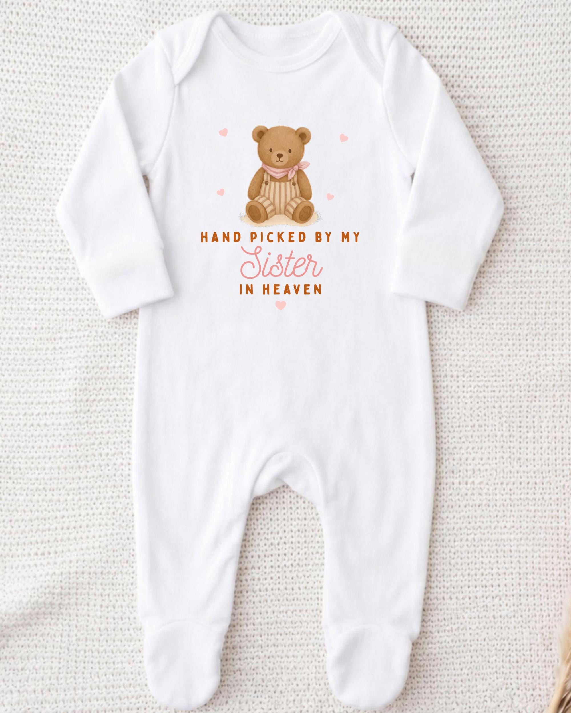A white onesie with a teddy bear graphic and the text "Hand picked by my Sister in Heaven" printed on it.