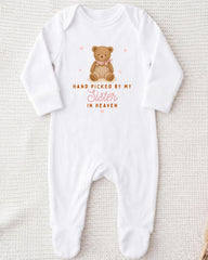 A white onesie with a teddy bear graphic and the text "Hand picked by my Sister in Heaven" printed on it.