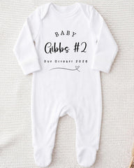 A white onesie with text printed on it, indicating the announcement of a baby's gender.
