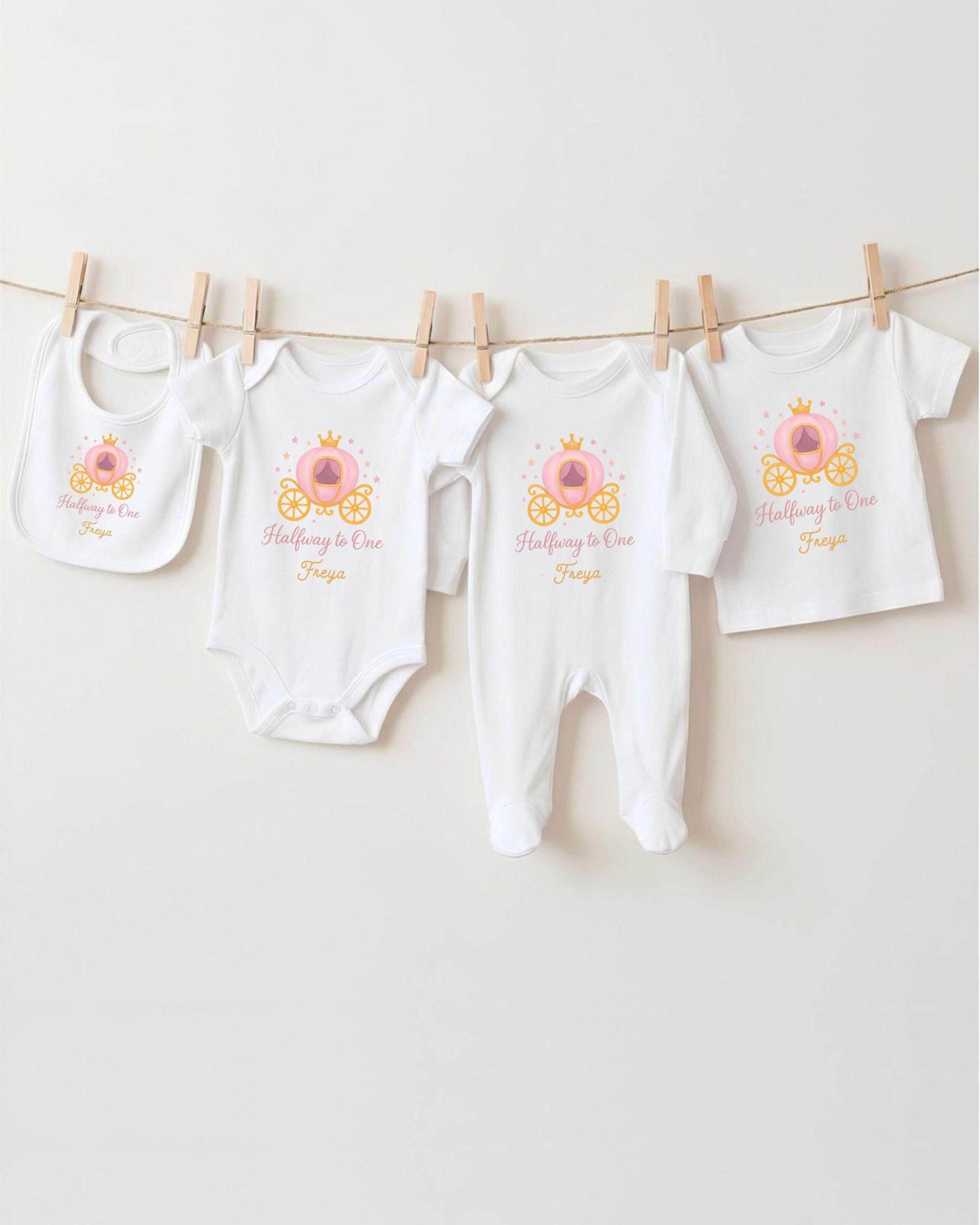 A row of four white baby clothes with a princess-themed design, including a princess carriage, is hanging on a clothesline.