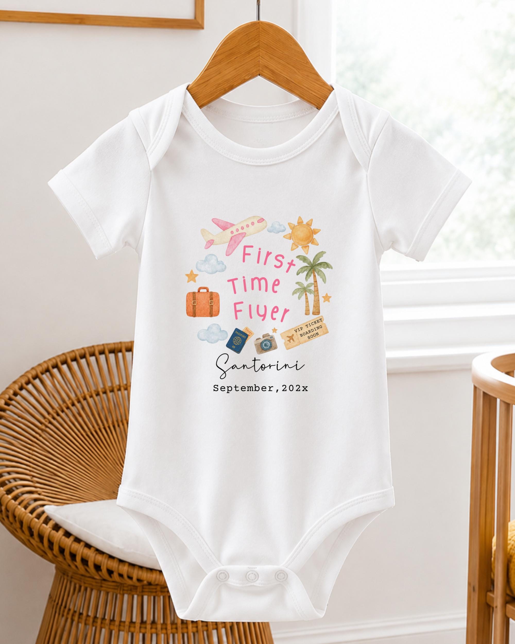A white baby onesie with a graphic design on it, hanging on a wooden hanger.