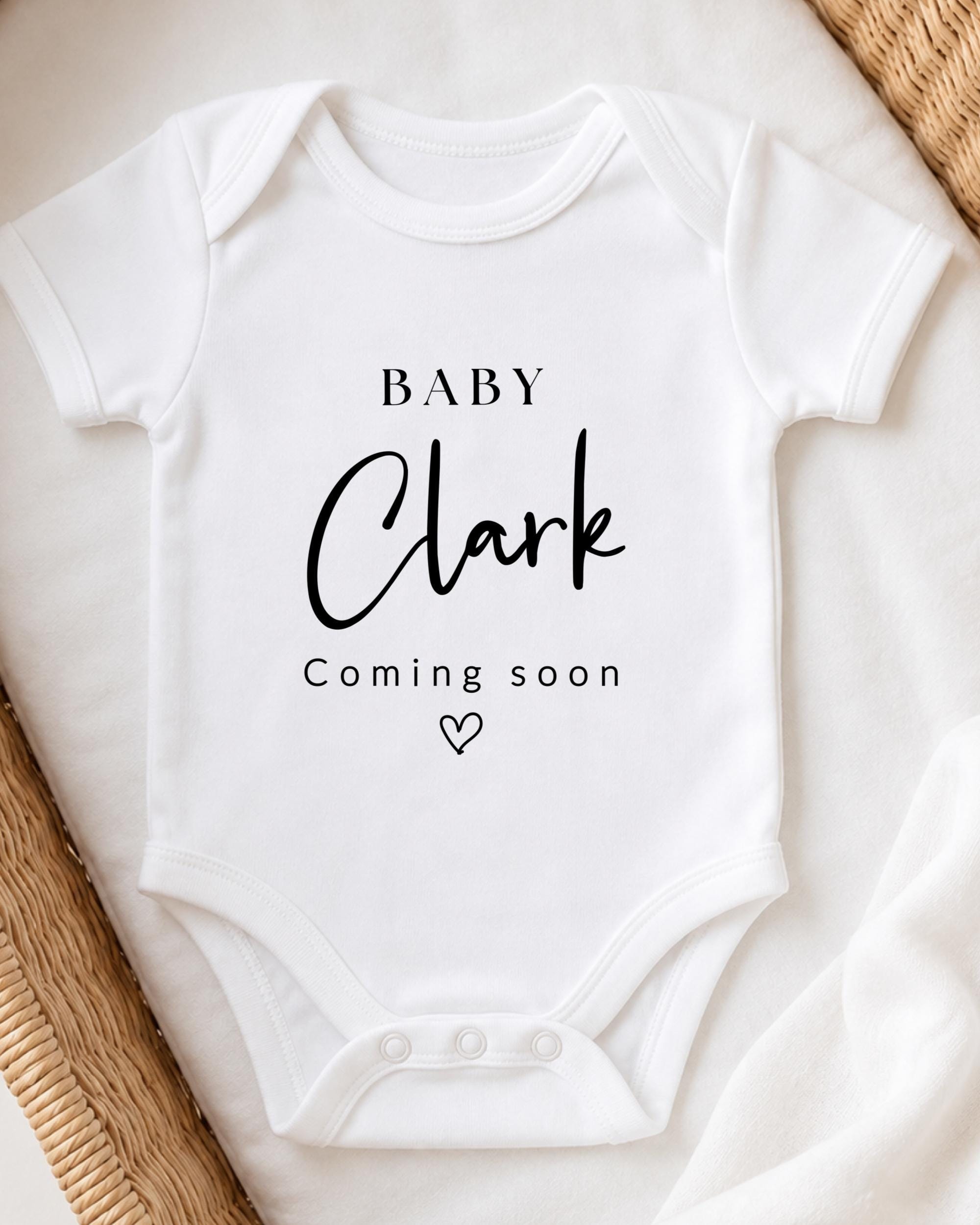 A white baby onesie with the text "BABY Clark" printed on it, along with the text "Coming soon" below it.
