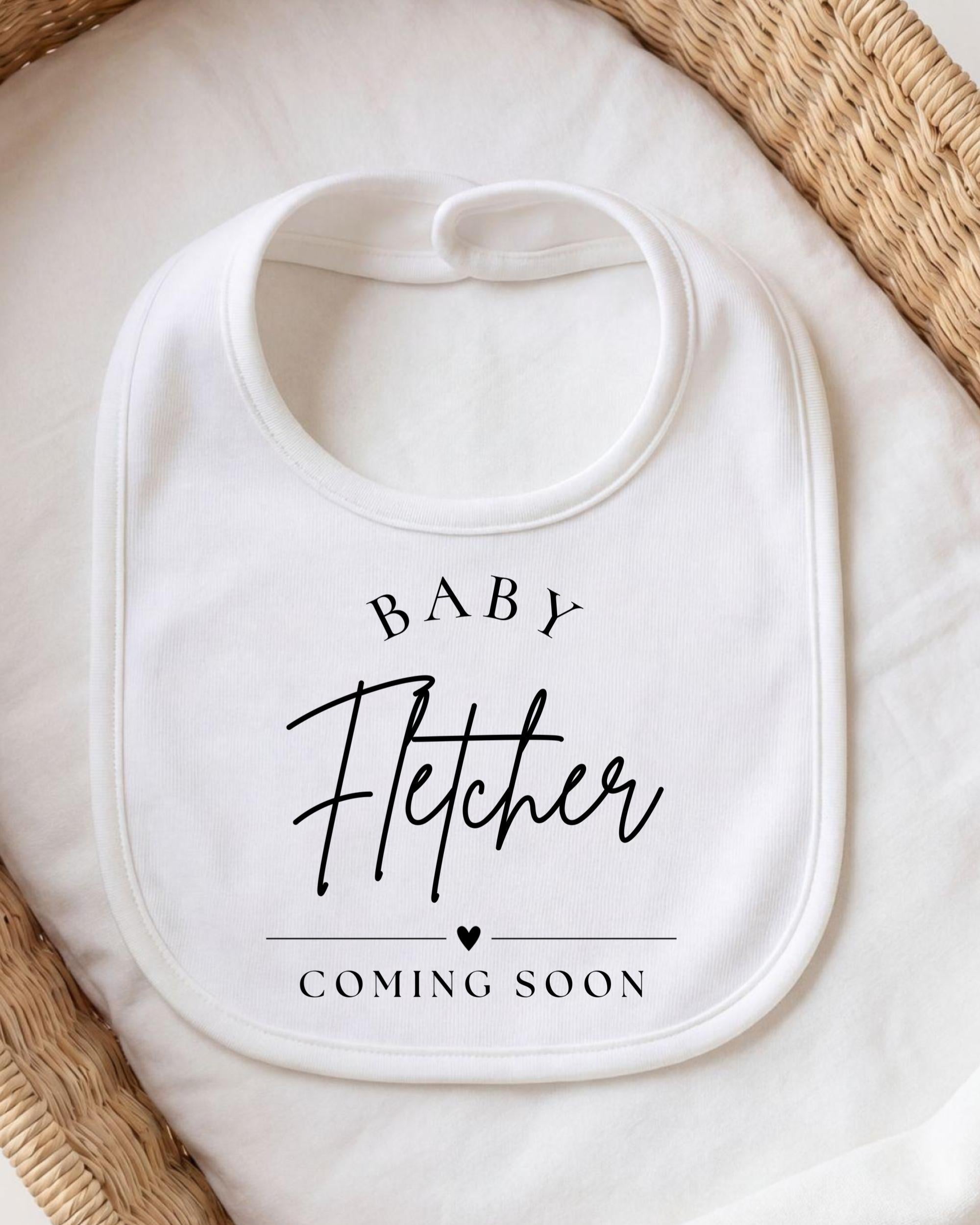 A white baby bib with the text "BABY FETCHER COMING SOON" printed on it.