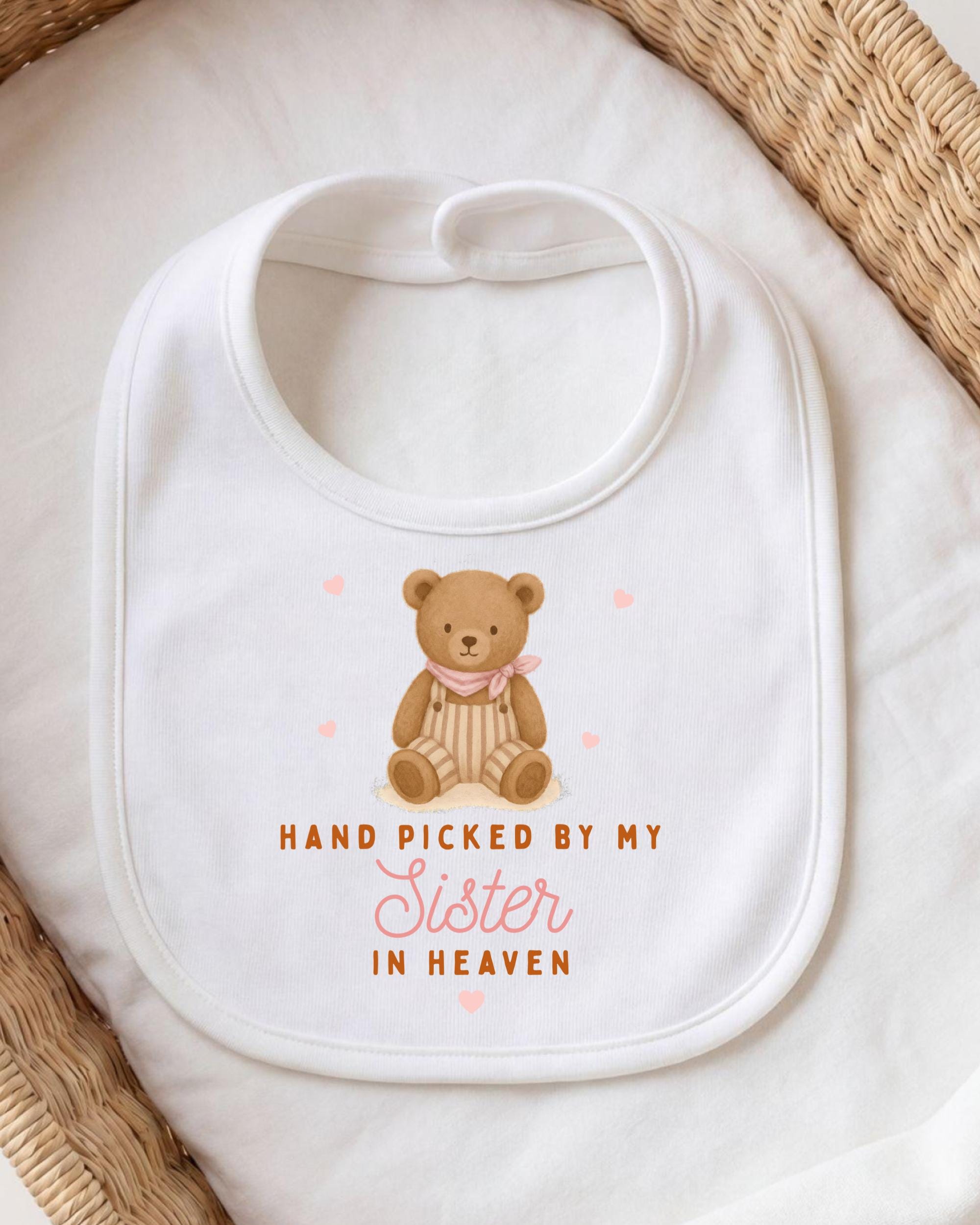 A white bib with a teddy bear and the text "HAND PICKED BY MY SISTER IN HEAVEN" printed on it.