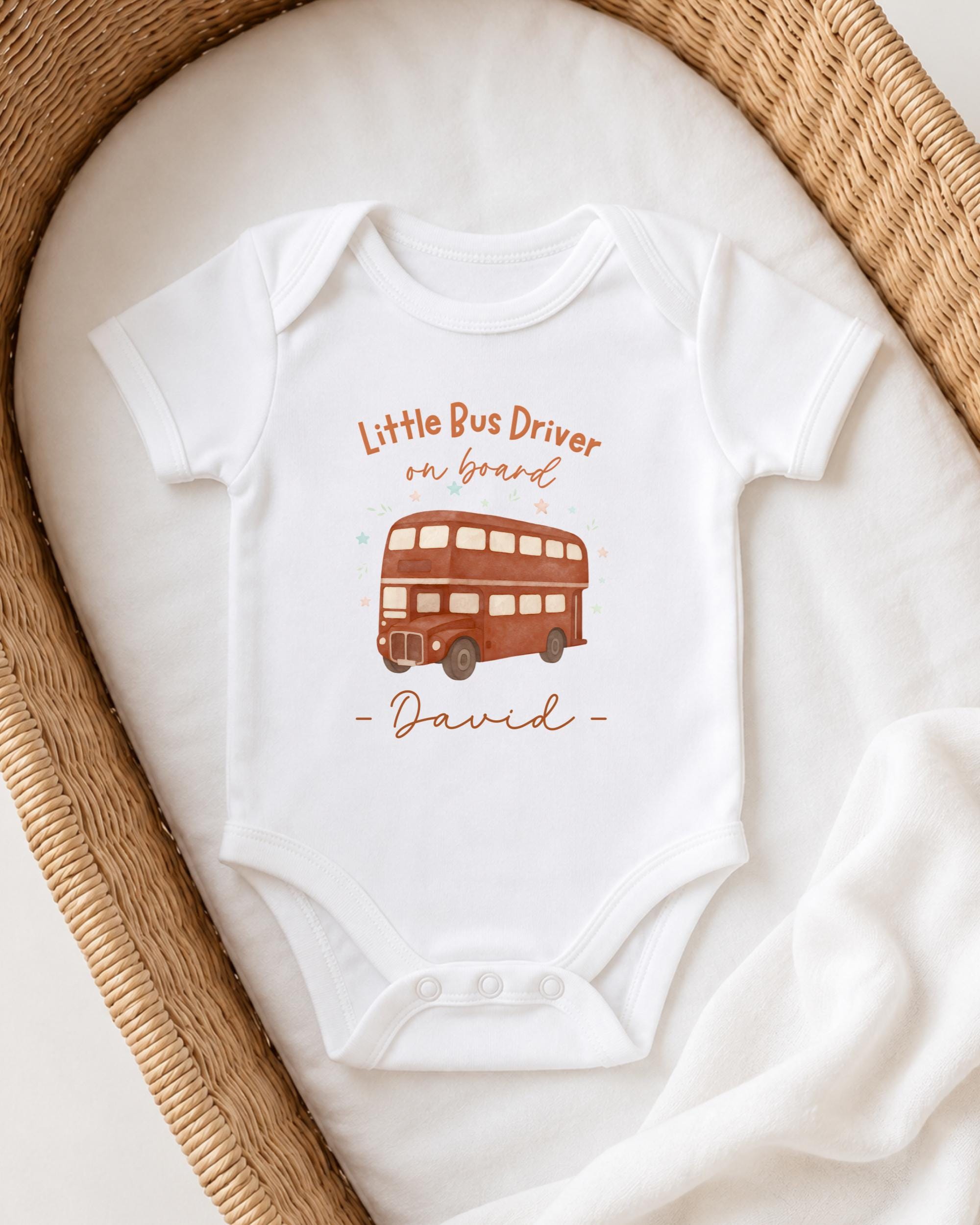 A white onesie with a printed image of a double-decker bus and the text "Little Bus Driver on board David" printed on it.