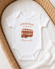A white onesie with a printed image of a double-decker bus and the text "Little Bus Driver on board David" printed on it.