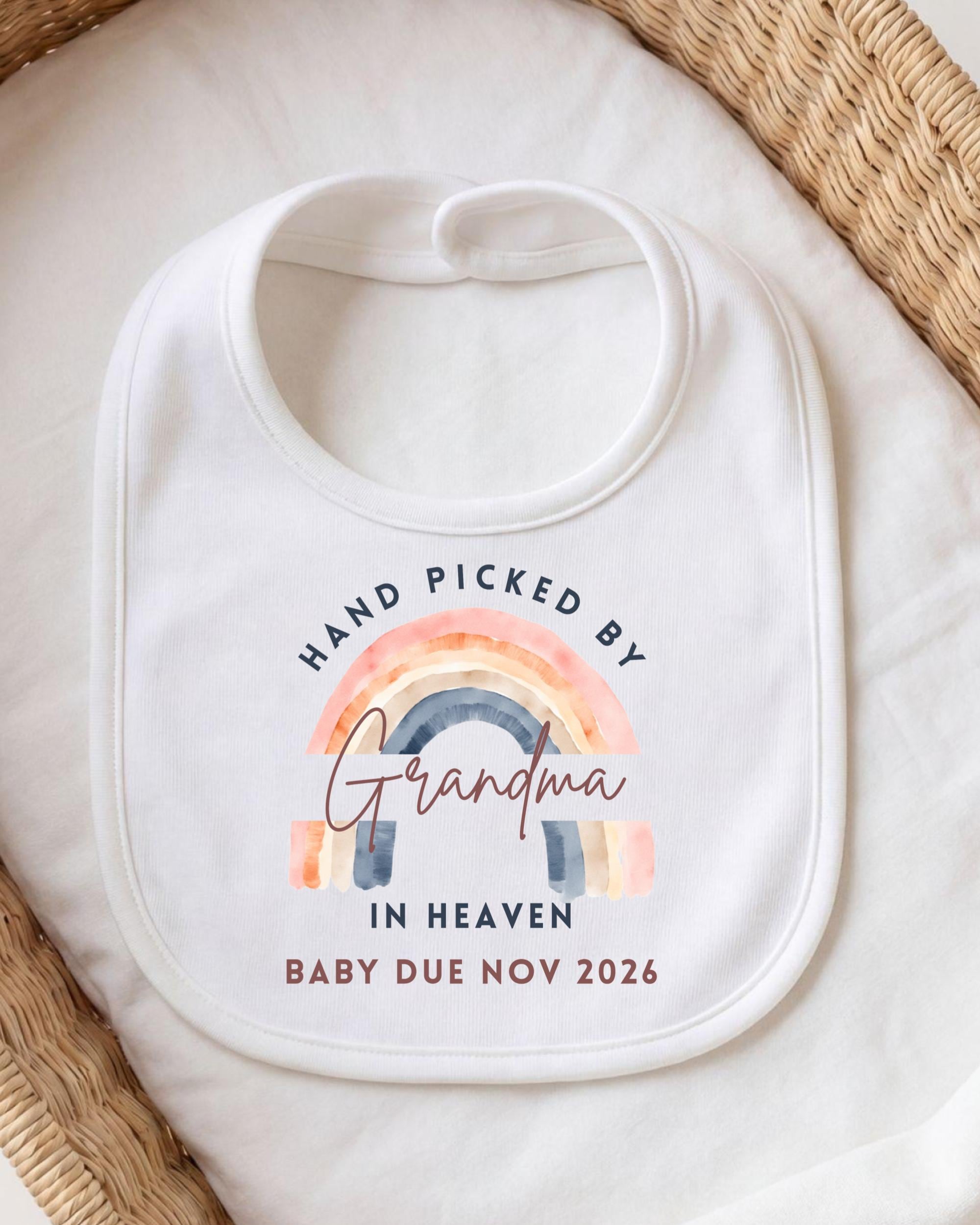 A white bib with a rainbow graphic and text that reads "Hand Picked by Grandma in Heaven Baby Due Nov 2026".