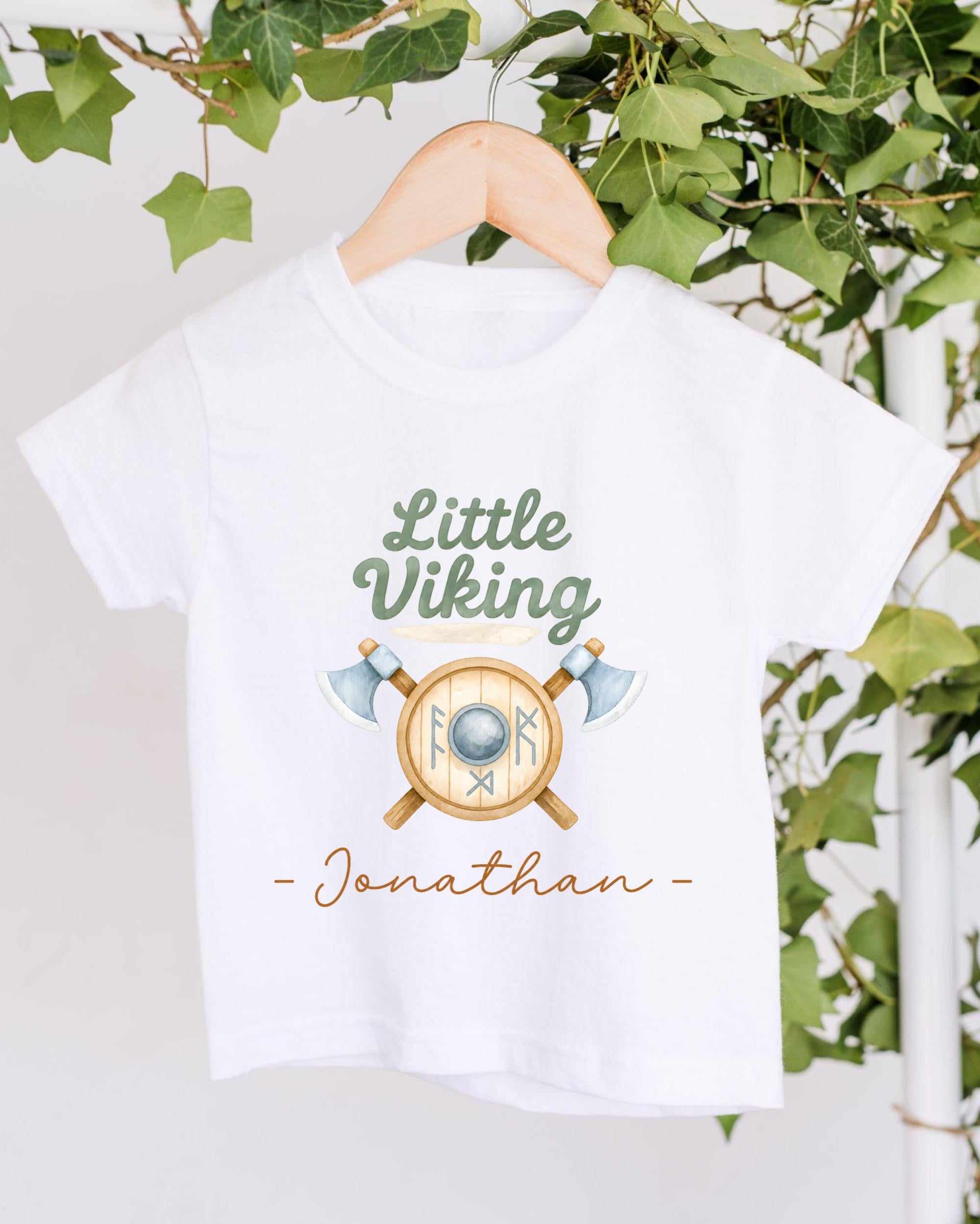 A white t-shirt with a graphic design featuring a shield and crossed axes, along with the text "Little Viking Jonathan" printed on it.