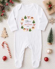 A white onesie with a Christmas wreath design, surrounded by various Christmas decorations such as a small Christmas tree, ornaments, and a candy cane.